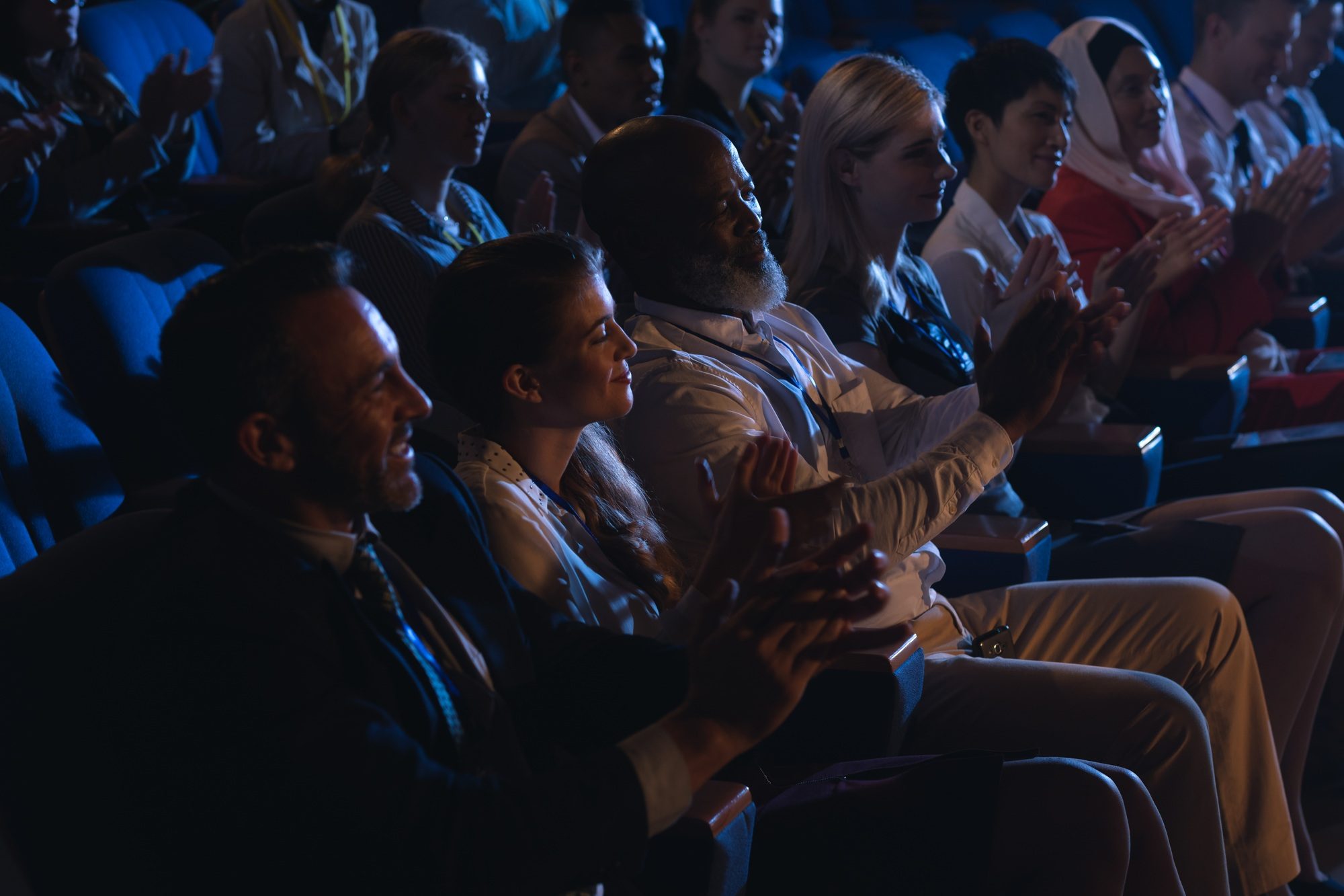 Business colleagues sitting and watching presentation with audience and clapping hands